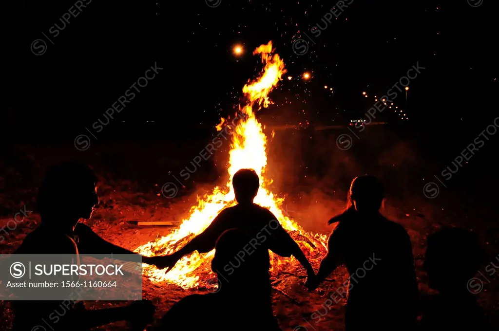 Children are holding hands and dancing in a circle around a bonfire
