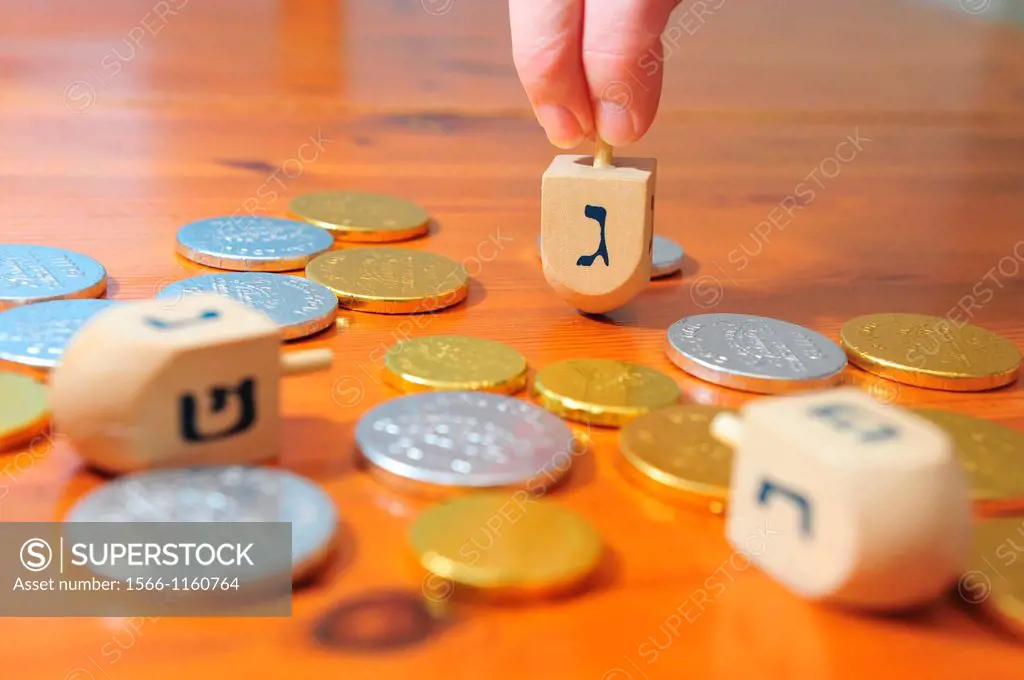 Photo of someone spinning a spinning top dreidel and gelt candy coins for Hanukkah