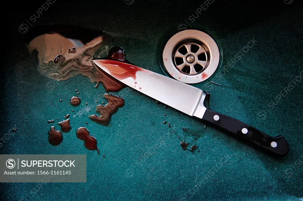 A knife with drops of blood on it resting in a dark green sink