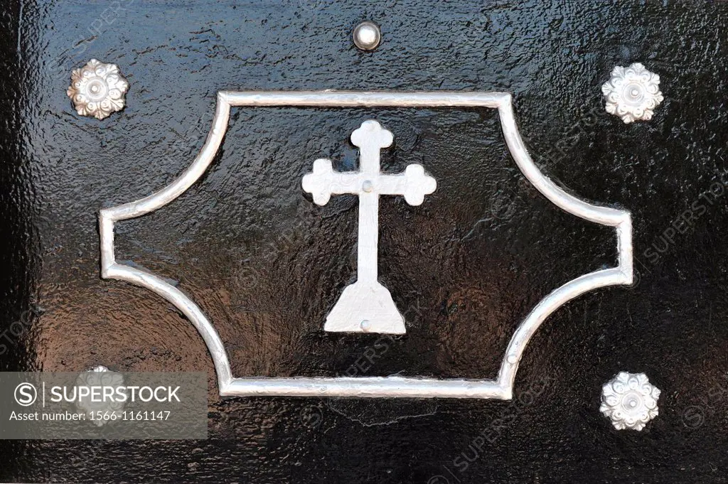A white cross and ornaments on a black painted door