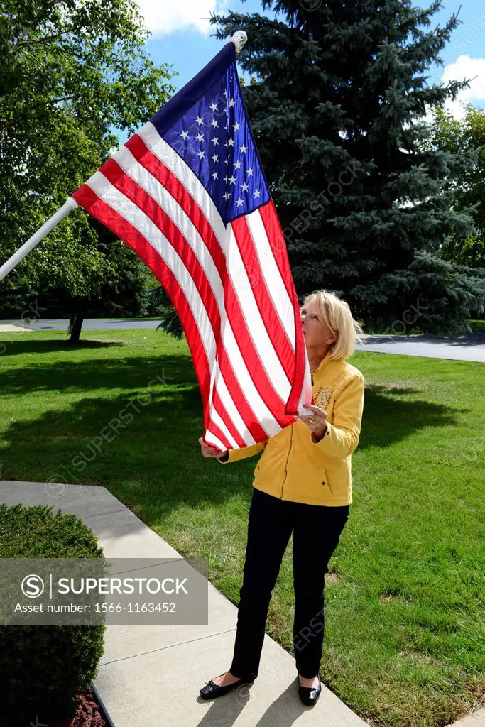 Woman straightens flag on flagpole in front of home