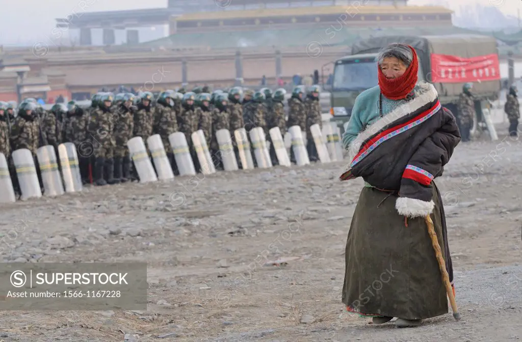 China, Gansu, Amdo, Xiahe, Monastery of Labrang Labuleng Si, Losar New Year festival, Old tibetan devotee in prayer and Chinese riot police