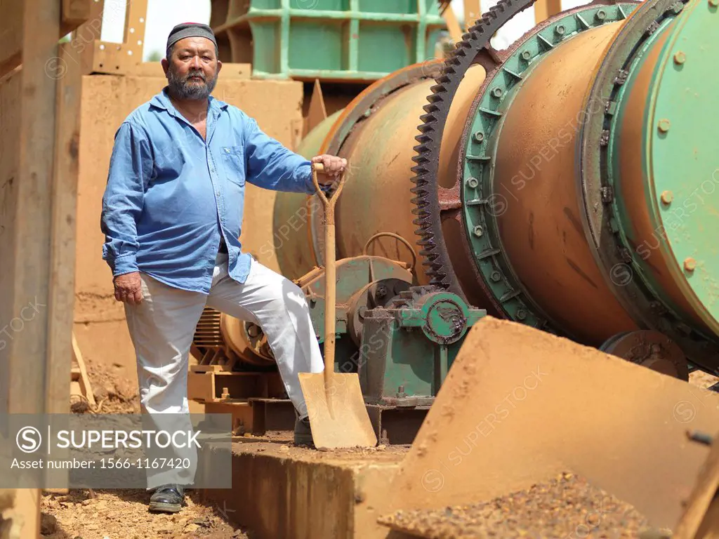 A project manager on a tin mining operation in Johor, Malaysia standing proudly next to heavy machinery used in the extraction.