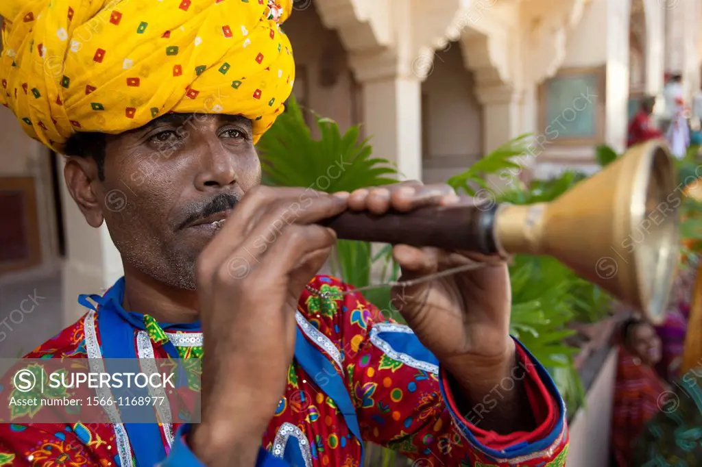 Male actor in turban playing horn Amber Fort near Jaipur Rajasthan India