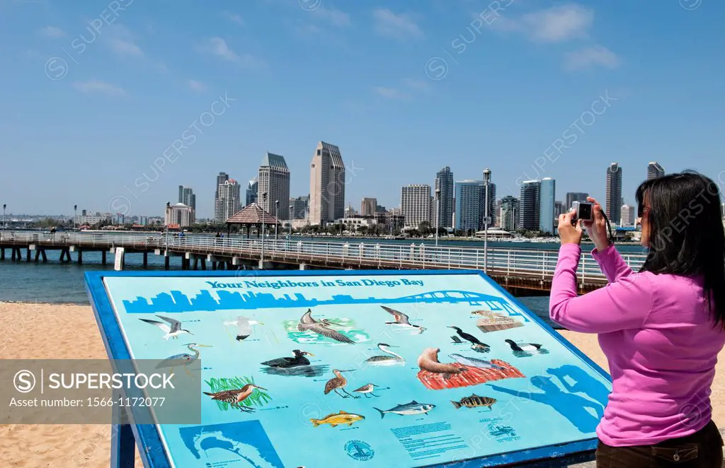 Woman taking photo of skyline of San Diego Bay California from Coronado Island showing water and buildings