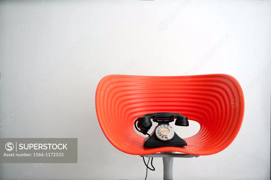 Telefono vintage encima de una silla moderna roja, Vintage telephone on top of contemporary red chair