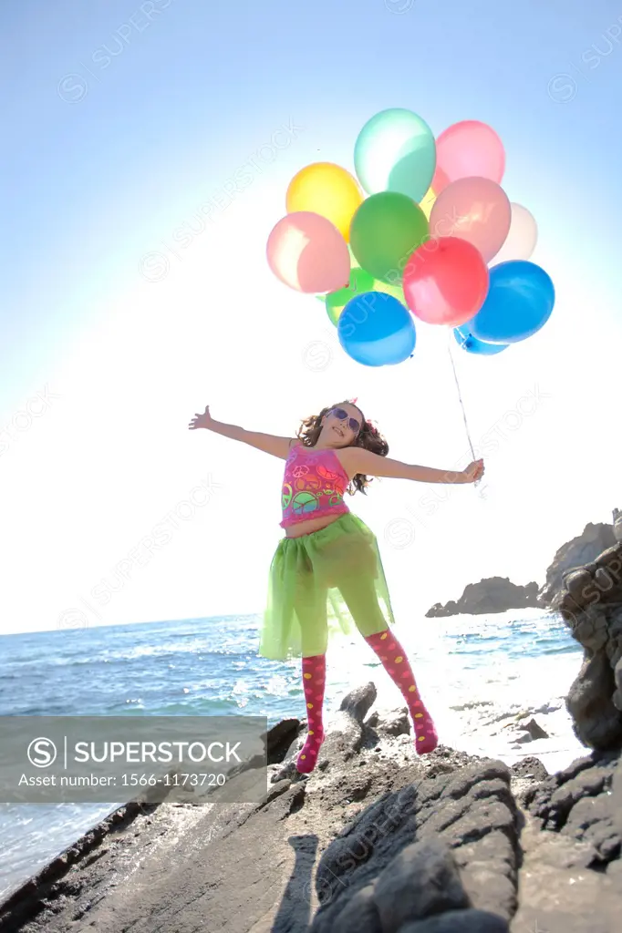 little girl jumping with joy holding balloons while at the ocean