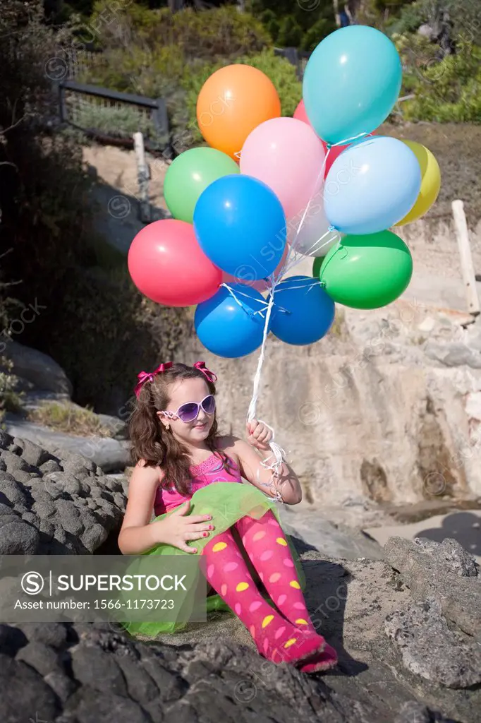 girl dressed up with balloons sitting on rocks