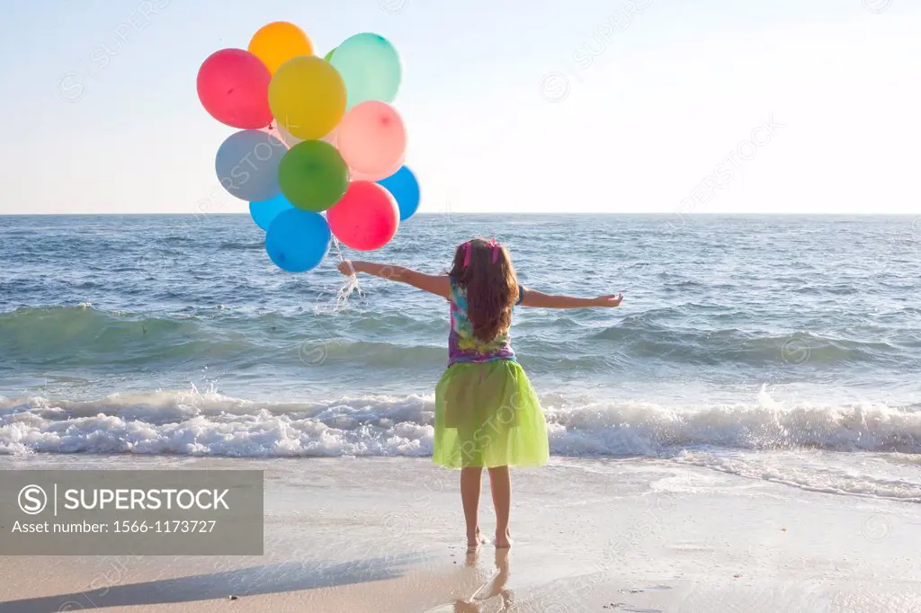 young girl standing at ocean with balloons