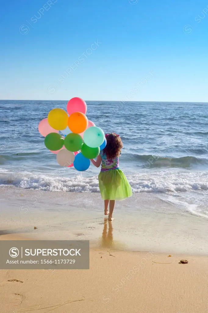 young girl walking towards the ocean with balloons with a view to see forever