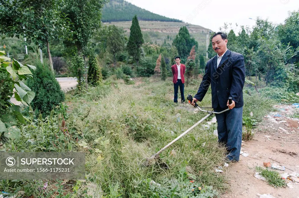 A funny man dressed in a sportcoat holding a strange shaped weed wacker or a string trimmer