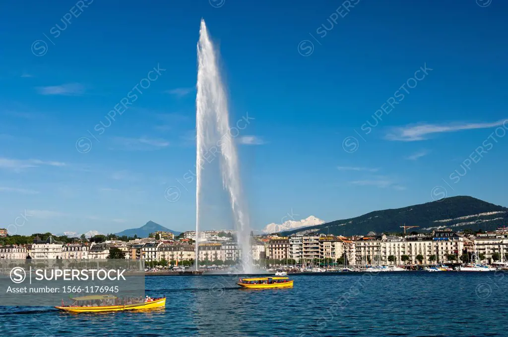 Yellow ferry boats of the company ´Mouettes Genevoises´ on Lake Geneva passing by the monumental water fountain Jet d´Eau, snowcovered Mont Blanc moun...