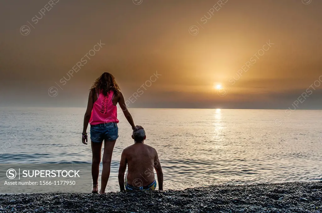 Europe, France, Corse, Haute Corse 2B, Cap Corse. Nonza. Black pebble beach. Girl and her father, at sunset.