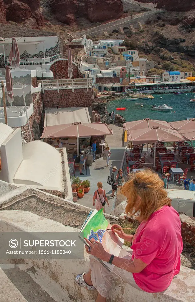 Artist painting scene at fishing village at bottom of Oia in Santorini in Greek Islands