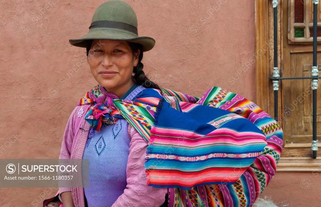 Traditional woman in dress and hat with baby on back in small town of Pisaq Peru
