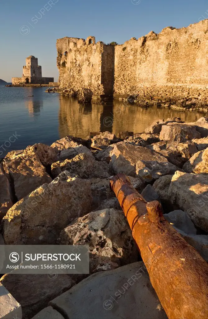 An old cannon lies on the rocks in front of The Venetian walls of Methoni fortress and the Bourtzi tower a small fortified island, Methoni, Messinia, ...