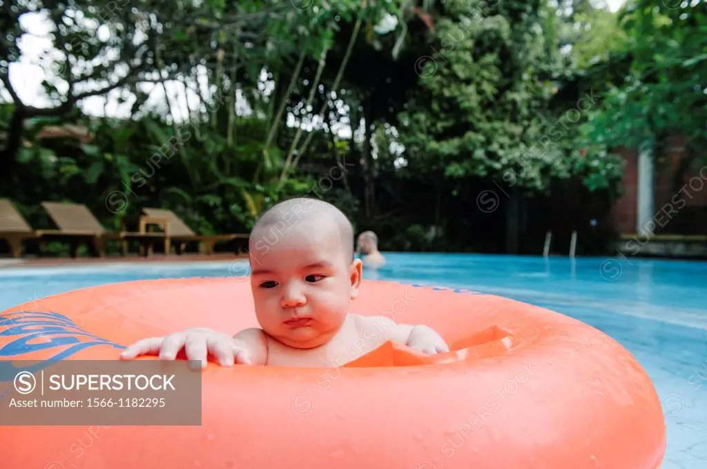 A mixed ethnicity child floats in an orange inner tube in a swimming pool