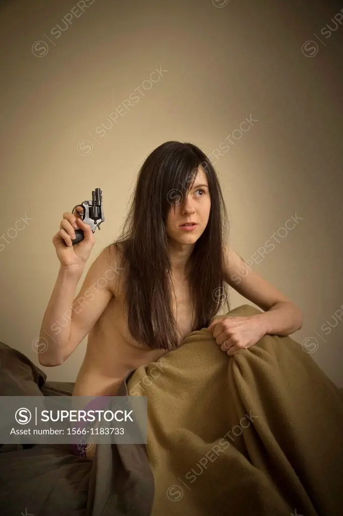 Young woman in bed, holding a gun