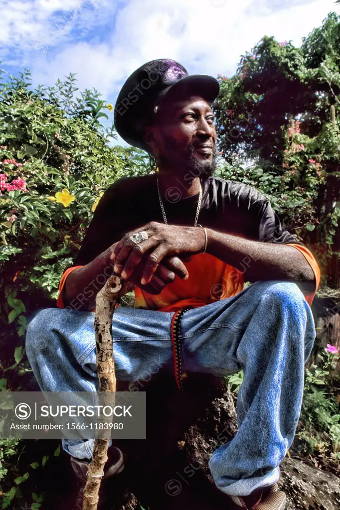 Reggae native man with hat and walking stick in colorful gardens near St John Antigua