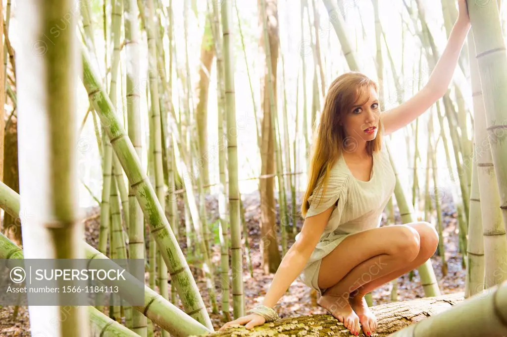 Portrait of a 30 year old redheaded woman wearing a white dress in a bamboo forest