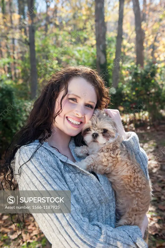 A 24 year old brunette woman holding and paling with Shih Tzu dog outdoors in the fall