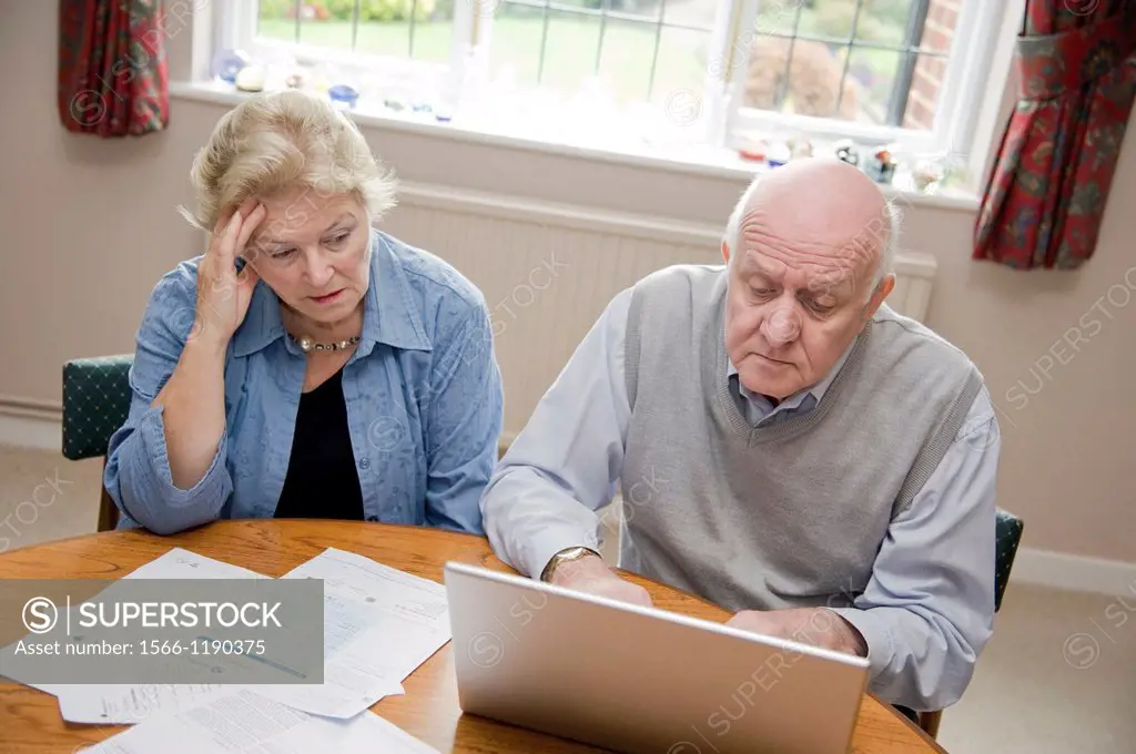 Mature couple using a laptop computer, worrying about their bills and debts online