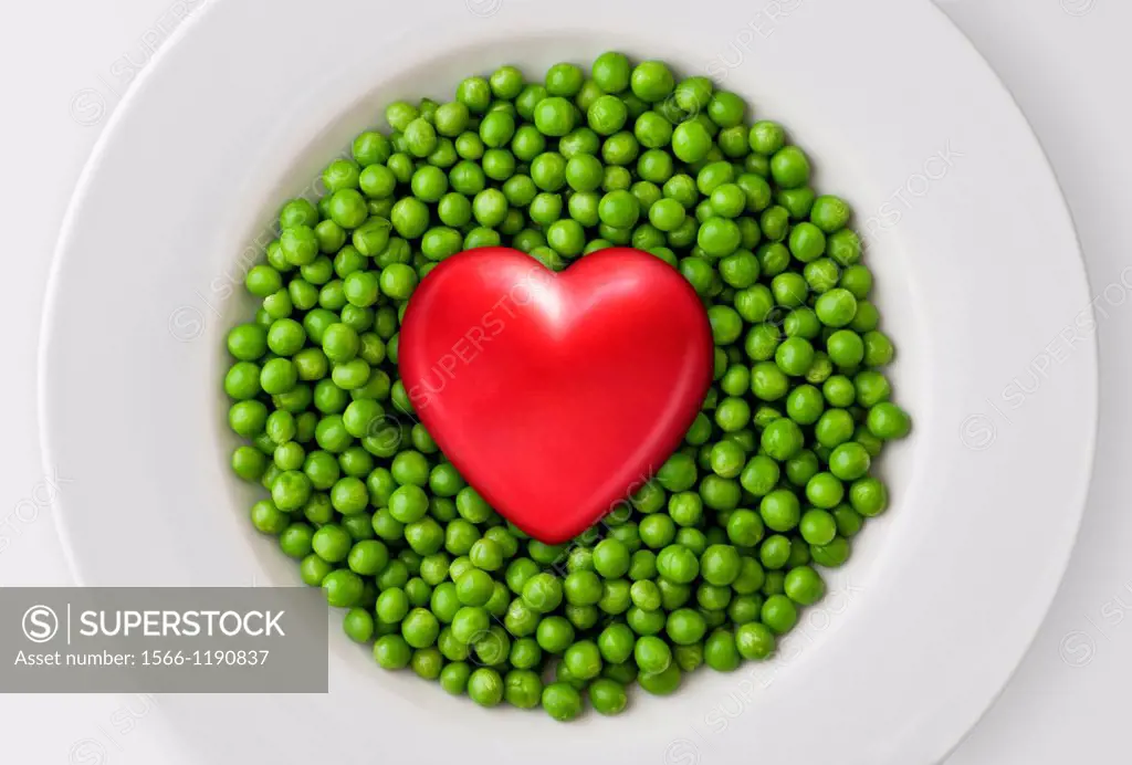 Red heart on fresh green peas  White plate, white background