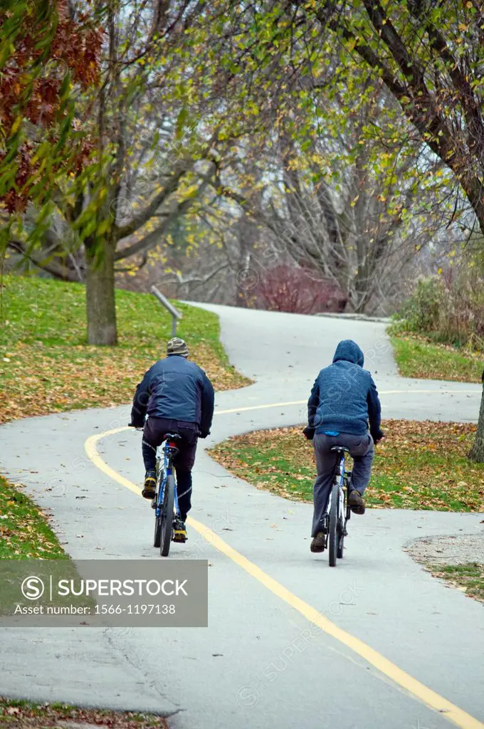 Two cyclists on a winding path in a public park on an autumn afternoon, Ontario, Canada