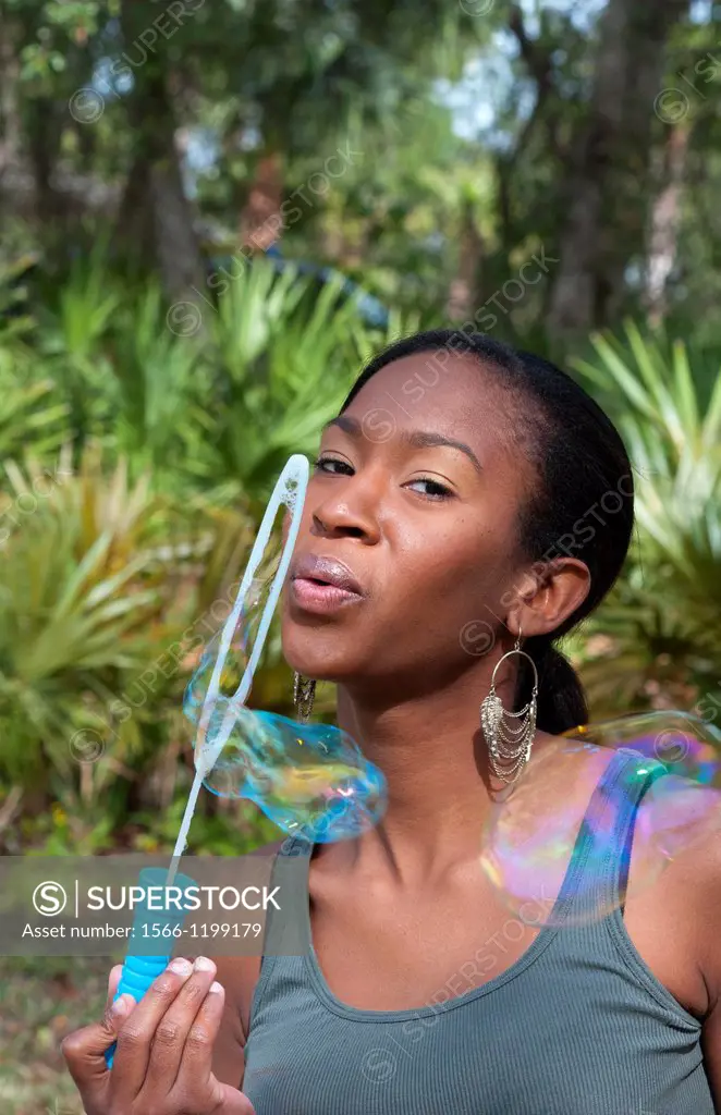 Black African American girl aged 18 blowing bubbles in yard outdoors laughing