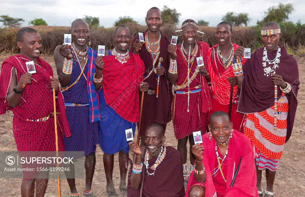 Kenya Africa Amboseli Maasai tribe village Masai group of men in red costume dress and beads holding Fuji Polaroids in remote area of Amboseli Nationa...