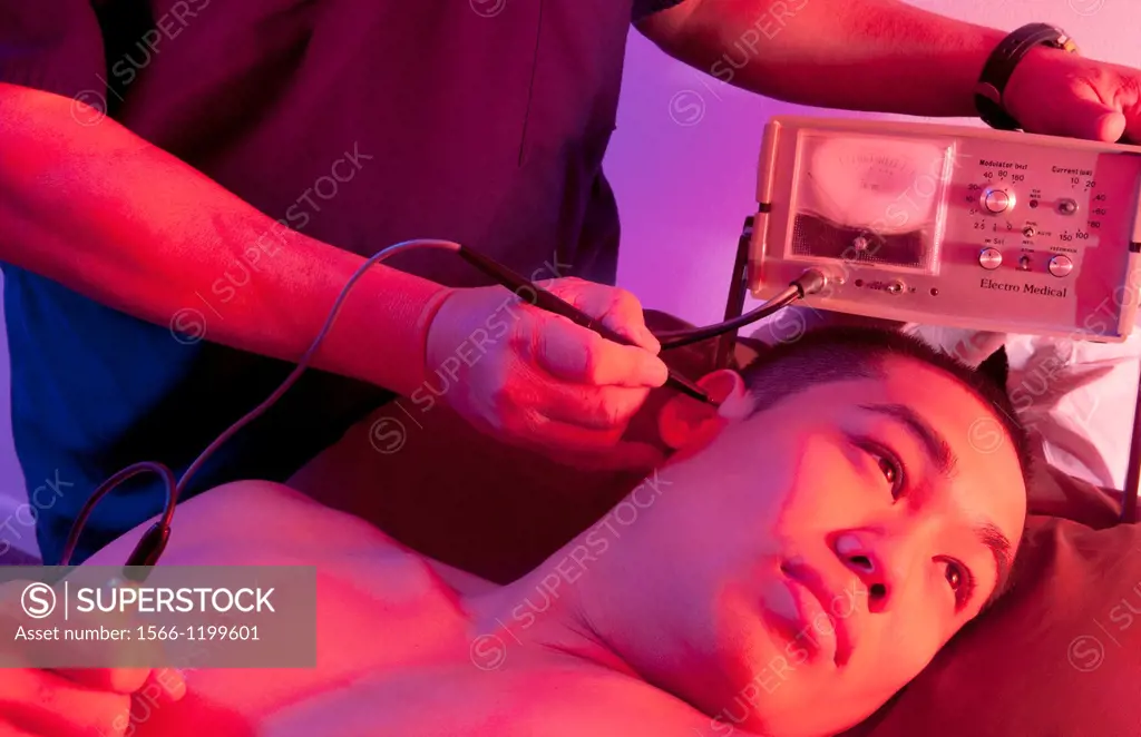 Chinese Acupuncture Doctor giving male patient acupuncture in ear with electronic vibrating stimulation with Stim Flex 400 machine