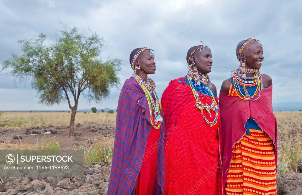 Kenya Africa Amboseli Maasai tribe village Masai women in red costume dress and beads and tree in remote area of Amboseli National Park safari 1