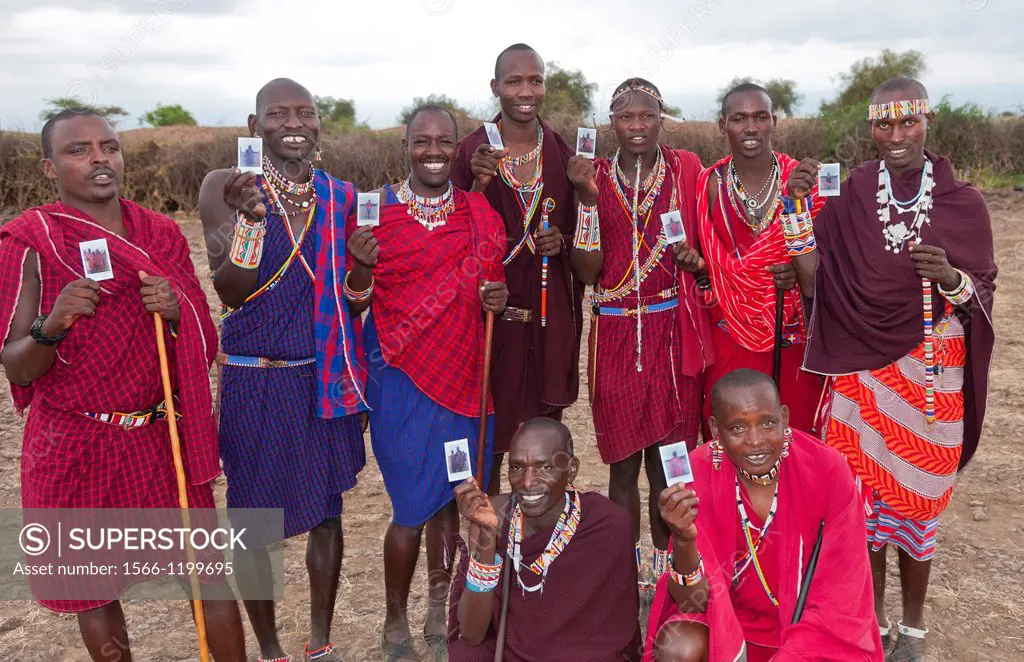 Kenya Africa Amboseli Maasai tribe village Masai group of men in red costume dress and beads holding Fuji Polaroids in remote area of Amboseli Nationa...