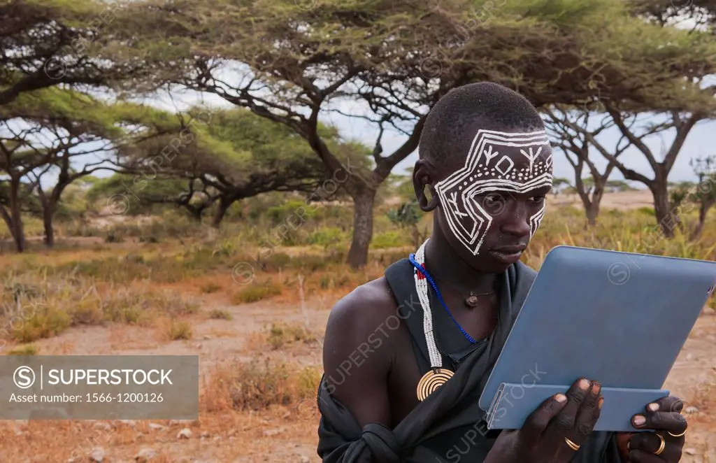 Tanzania Serengeti Africa Masai Maasai boy playing with Digital tablet computer in black clothes from circumcision ceremony with face paint 7