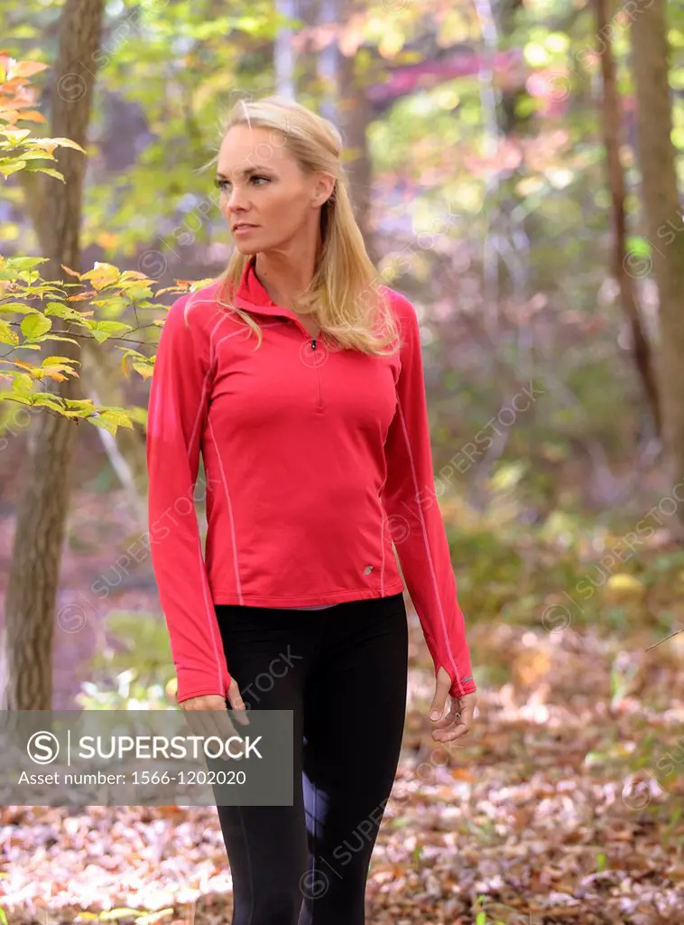 A 38 year old blond woman wearing work-out clothing walking through a forest setting in the fall