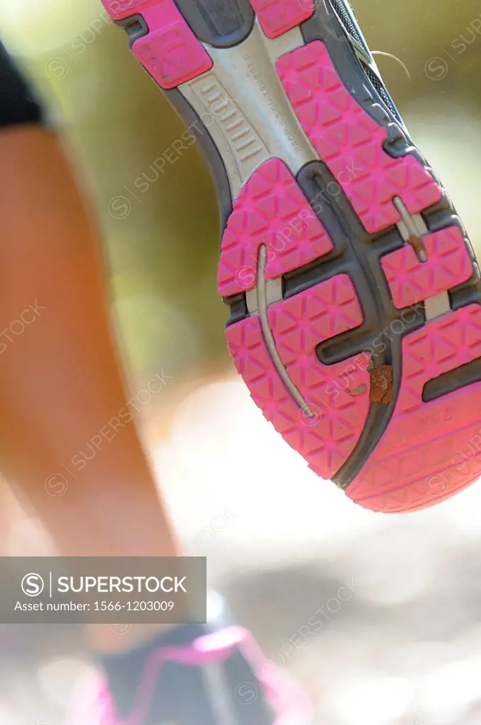 Close shot of the sole of a running shoe on a woman running through a forest