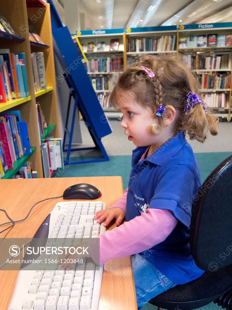 Three year old caucasian girl in preschool top using a computer in a public library.
