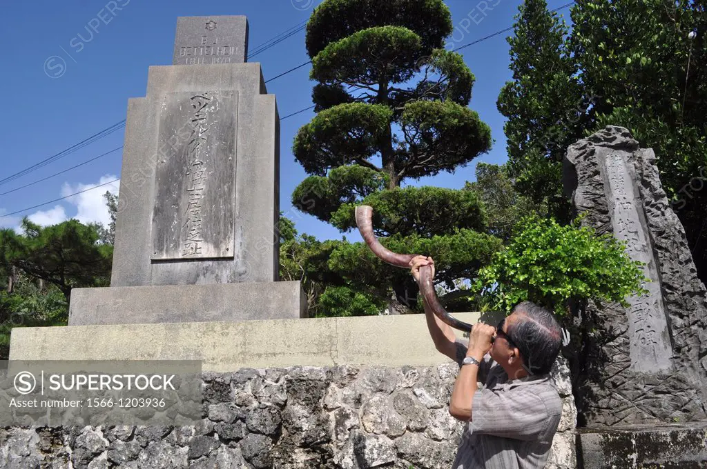 Naha, Okinawa, Japan, a Christian man blowing a horn to honor the missionary that brought Christianity to Okinawa, by his grave at Gakokuji Temple