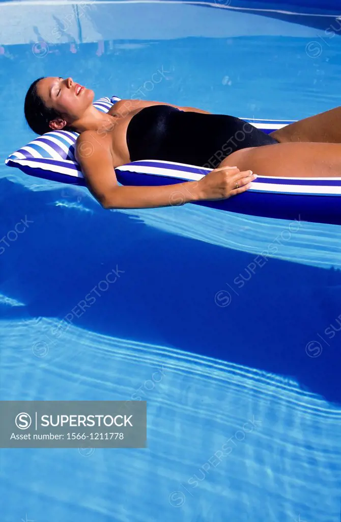 Pregnant woman sunbathing on mattress in swimming pool