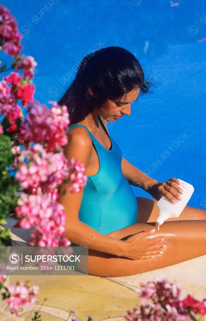 Pregnant woman creaming her legs at swimming pool side