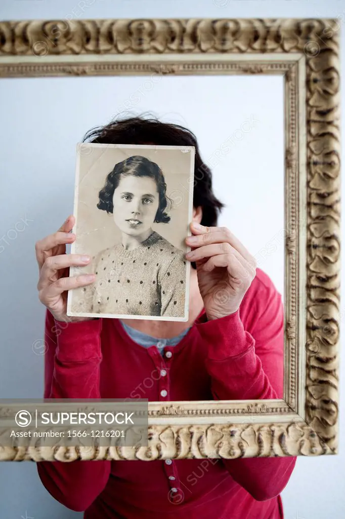 Mujer joven dentro de un marco dorado con retrato antiguo en las manos tapandole la cara, Young woman in a gold frame with old picture in her hands co...
