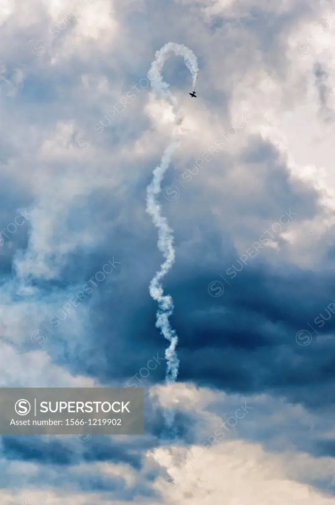 Single plane performing aerial aerobatics with a smoke trail against a moody sky backdrop