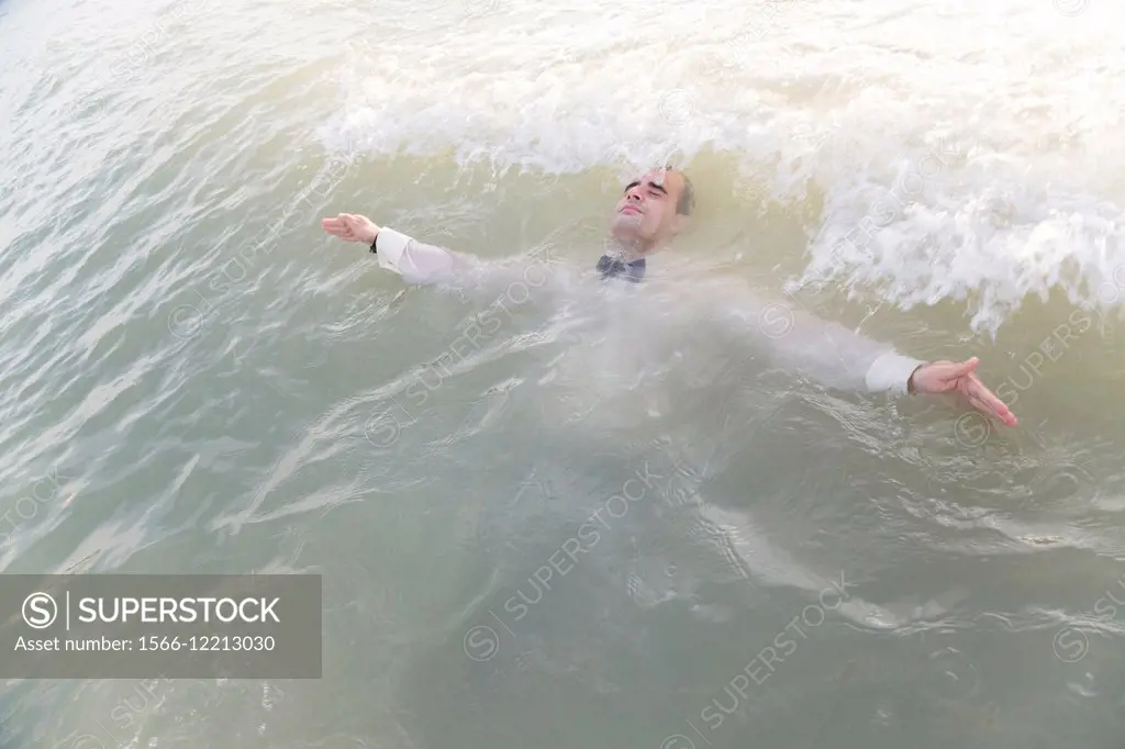 Dressed up young man surrendering to sea waves
