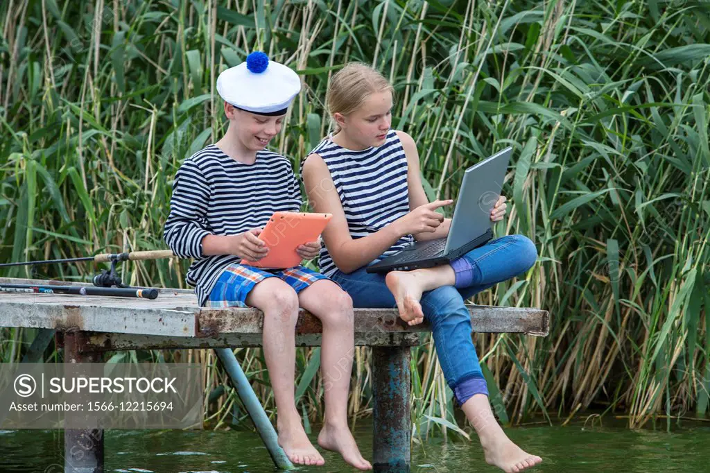 Boy and girl of twelve years in a sailor uniform with a laptop on the dock.
