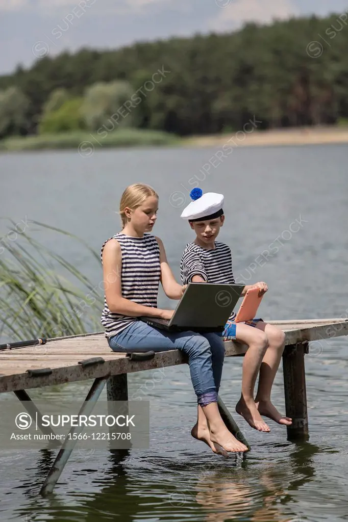 Boy and girl of twelve years in a sailor uniform with a laptop on the dock.
