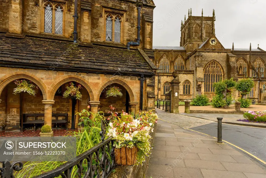 Almshouse and Abbey, Sherborne, foreshortening of medieval buildings in historic town center with some flowers in foreground.