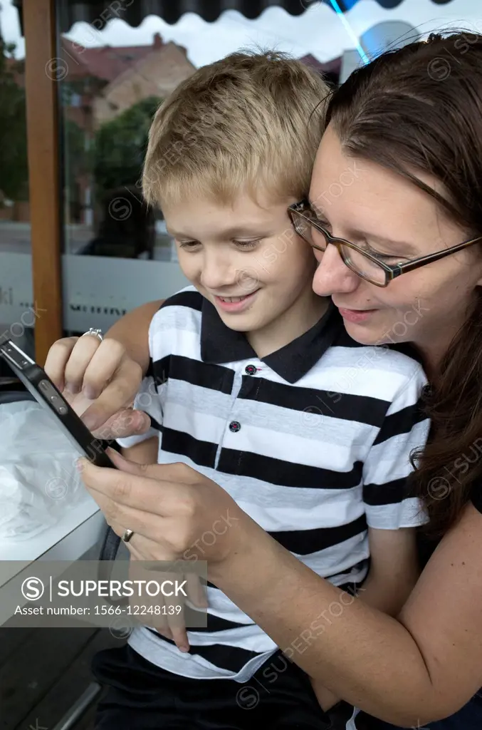 Polish mom and son age 10 and 34 playing on her cell phone. Rawa Mazowiecka Central Poland.
