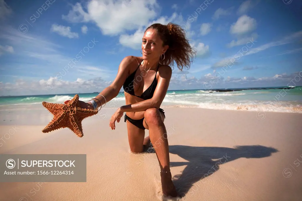 Woman holding a starfish on the beach, Isla Mujeres, Cancun, Quintana Roo, Yucatan Province, Mexico, Central America.