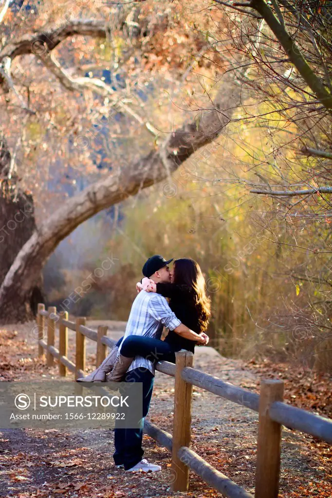 Couple embracing, kissing in the forest, sitting on a fence with scenic fall colors