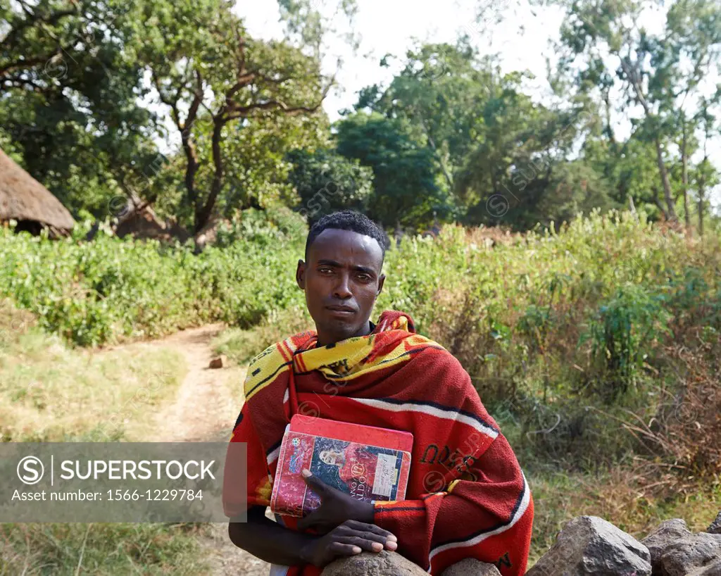 A local villager dressed in red and carrying books standing inside the church grounds of the Zara Church Forest in Ehtiopia, Africa